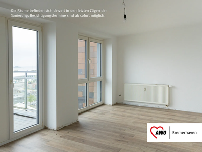 Heller leerer Raum mit großen Fenstern, Holzboden, Heizkörper an der Wand und Zugang zu einem Balkon mit Glasgeländer. | © AWO Bremerhaven